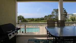 A covered patio with a grill, a table, and chairs overlooking a pool and ocean view. - Dunes Club 1D (Port St. Joe)