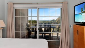 A hotel room with a bed, a TV, a window with curtains, and a view of a beach. - Dunes Club 1D (Port St. Joe)