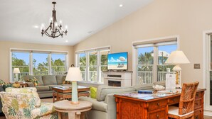 A spacious living room with a large window, a television, a chandelier, and a dining area. - Sweet Home Apalachee (Port St. Joe)