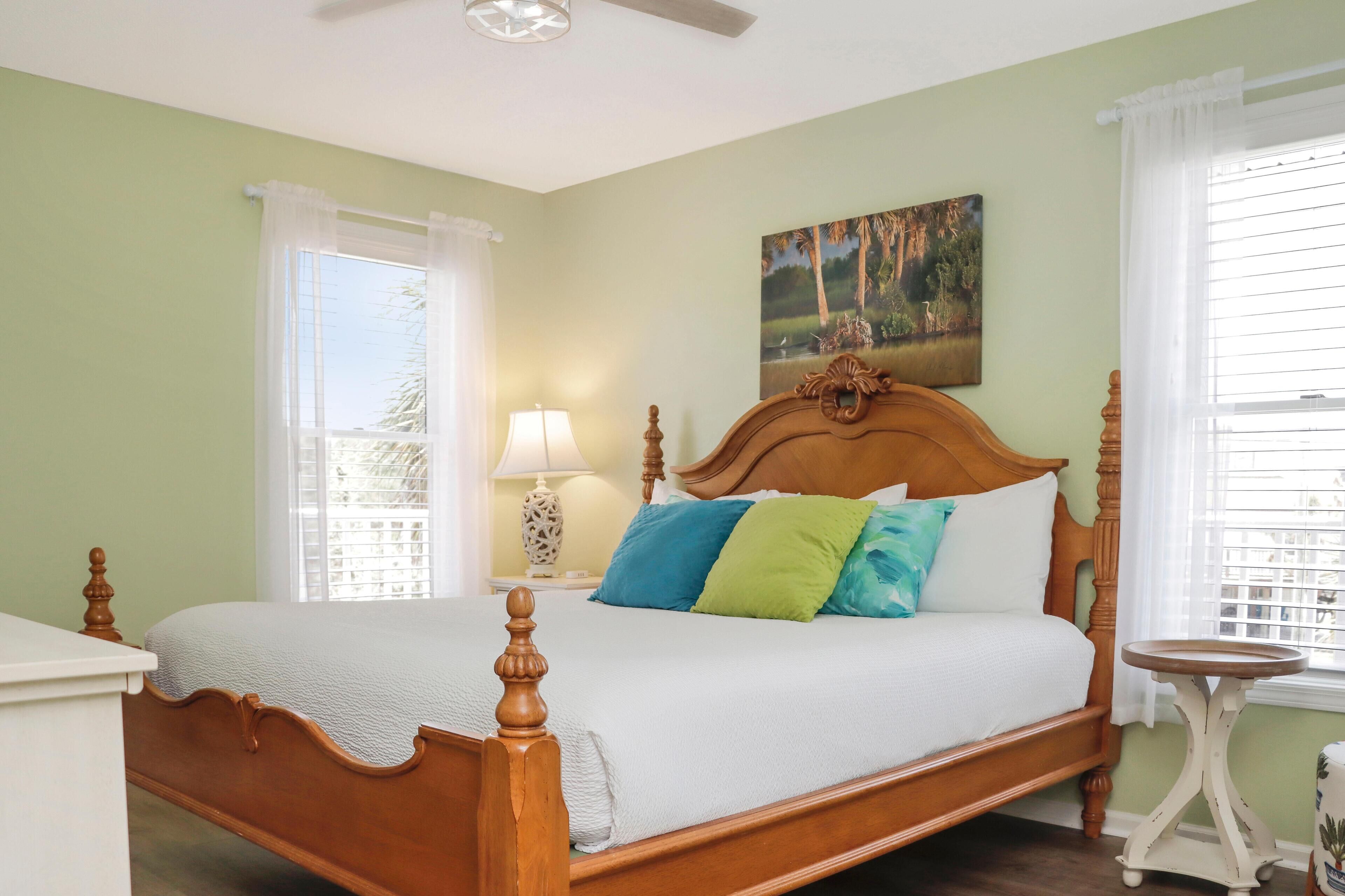 Un dormitorio con cama de madera, paredes verdes y un cuadro sobre la cama.