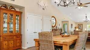 A dining area with a wooden table and wicker chairs, a wooden cabinet with glass doors, and a chandelier. - Sweet Home Apalachee (Port St. Joe)