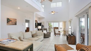 A spacious living area with a high ceiling, a ceiling fan, and a large window providing natural light. - Beach Please (Port St. Joe)