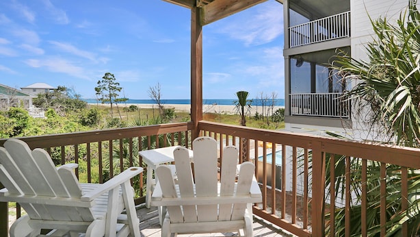 A wooden deck with white Adirondack chairs overlooking a beach and a two-story building with balconies. - Beach Please (Port St. Joe)