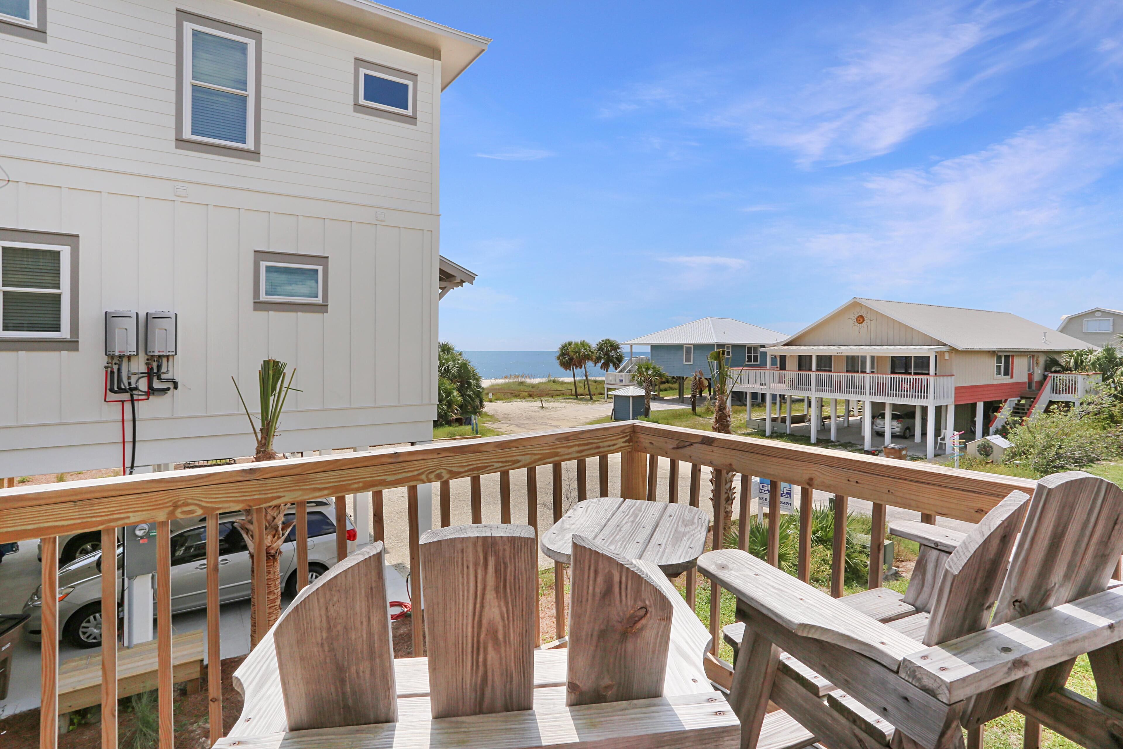 A wooden deck with chairs and tables, overlooking a beach and buildings.