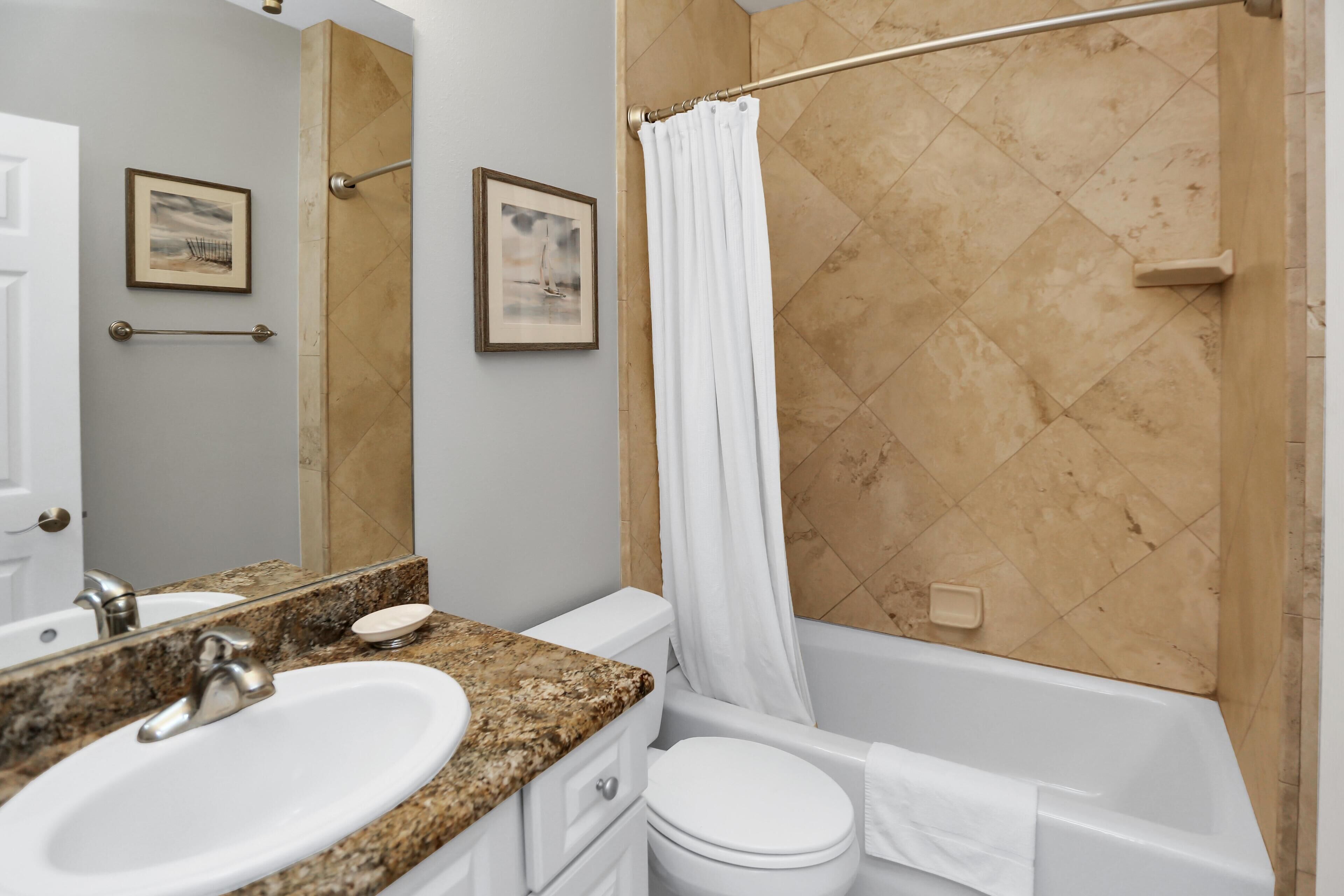 A bathroom with a granite countertop sink, a white toilet, a bathtub, and a shower curtain.
