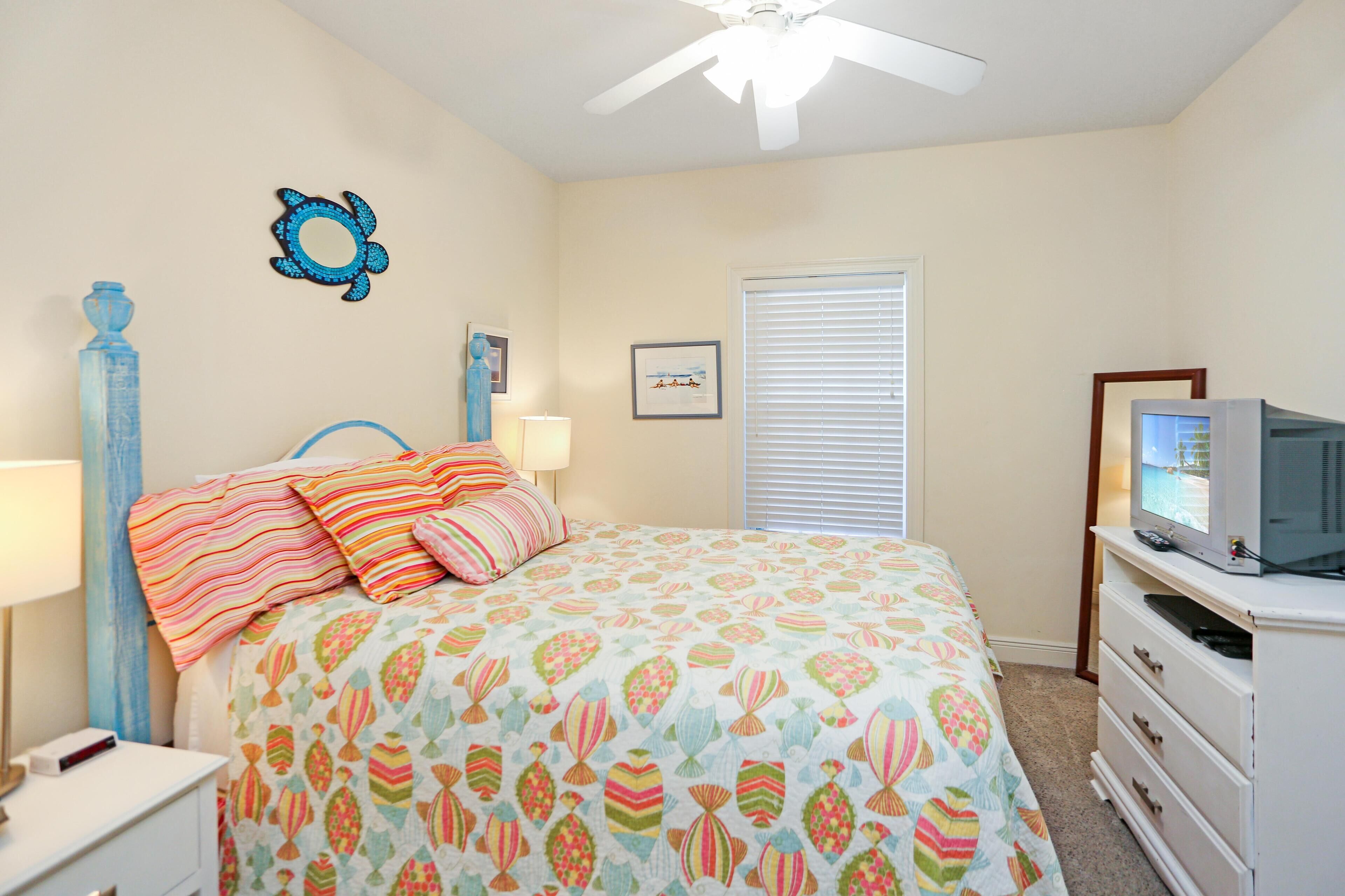 A bedroom with a bed, a ceiling fan, a TV, and a dresser.
