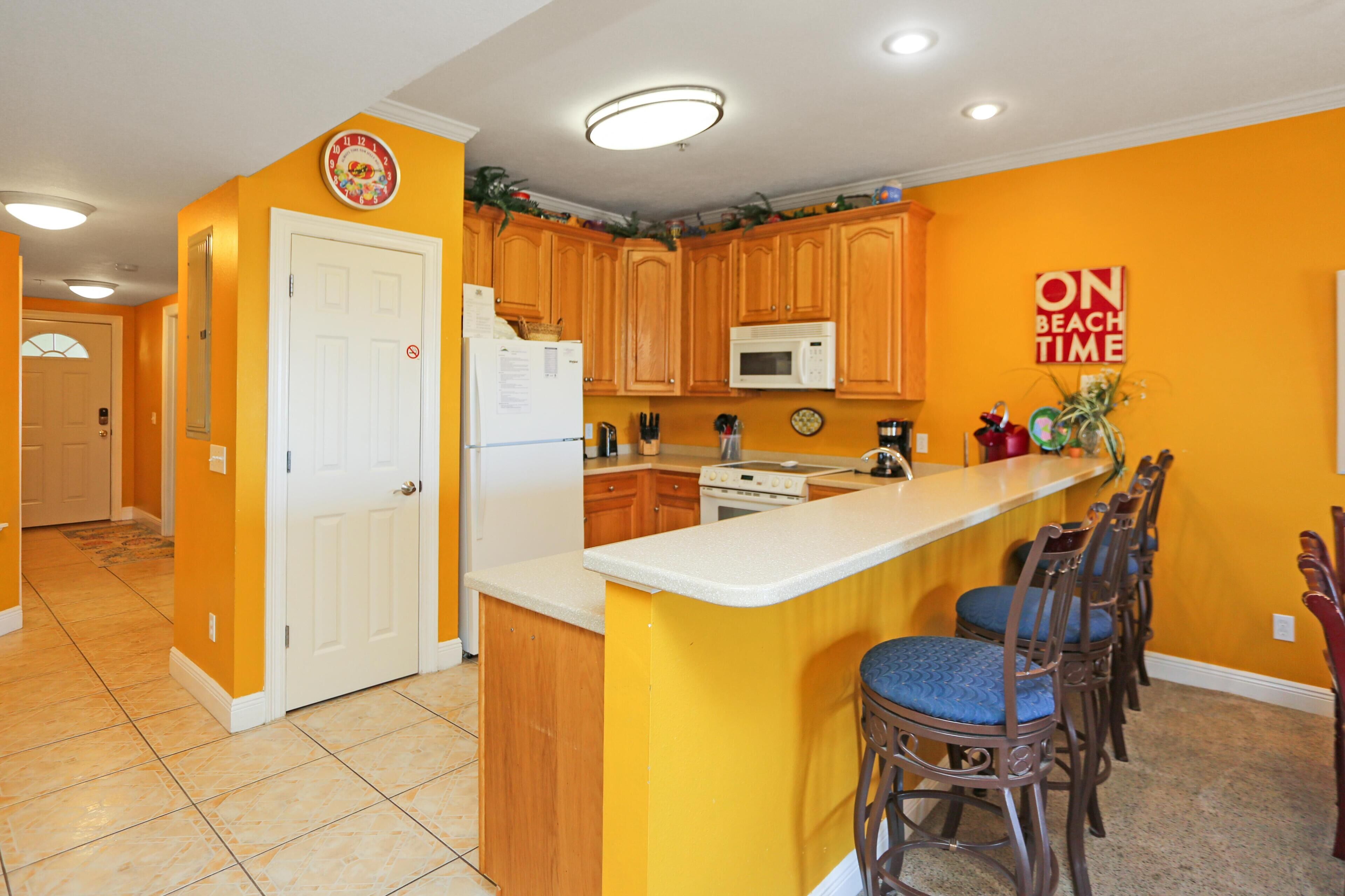 A kitchen with wooden cabinets, a white refrigerator, a microwave, and a bar area with stools.