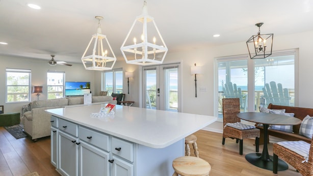A spacious kitchen with a large island, modern pendant lights, and a view of the ocean through large windows. - Brodie House (Port St. Joe)