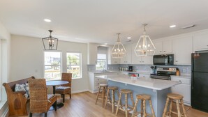 A modern kitchen with a central island, bar stools, and a dining area with wicker chairs. - Brodie House (Port St. Joe)