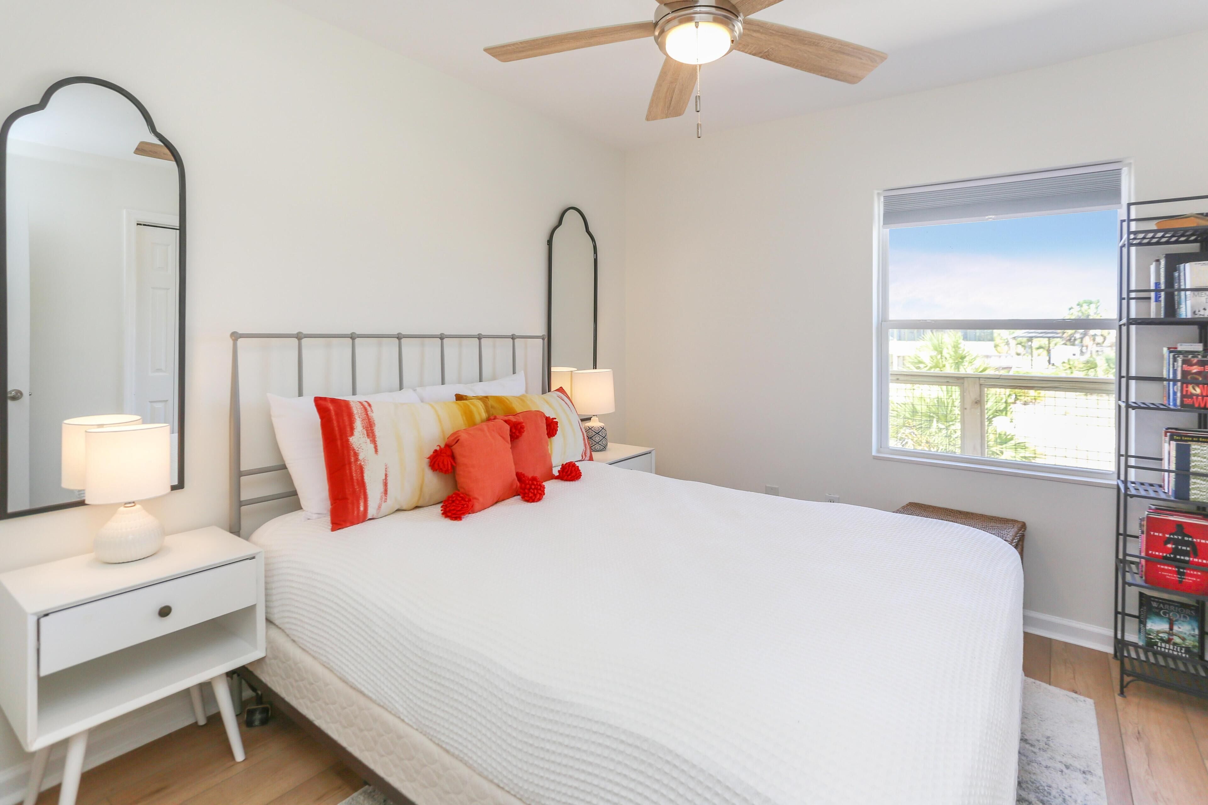 A bedroom with a bed, nightstands, a ceiling fan, a window, and a bookshelf.