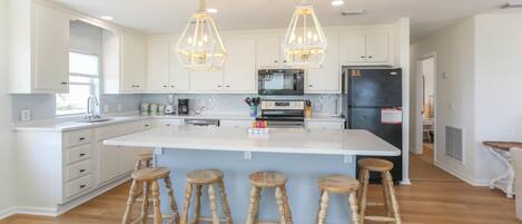 A modern kitchen with white cabinets, a central island with stools, and pendant lighting.