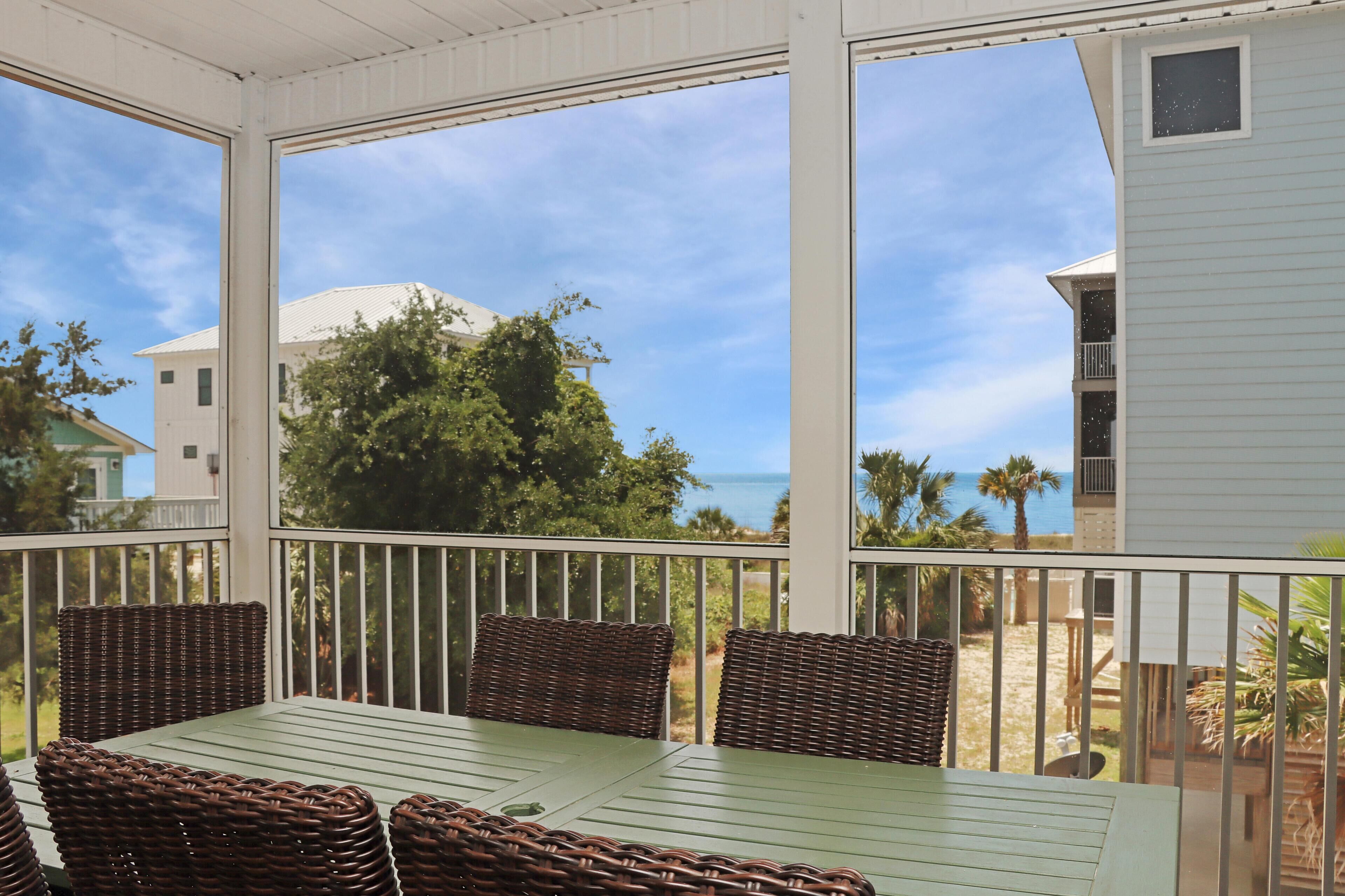 Un patio techado con una mesa y sillas, con vista a la playa y al océano.