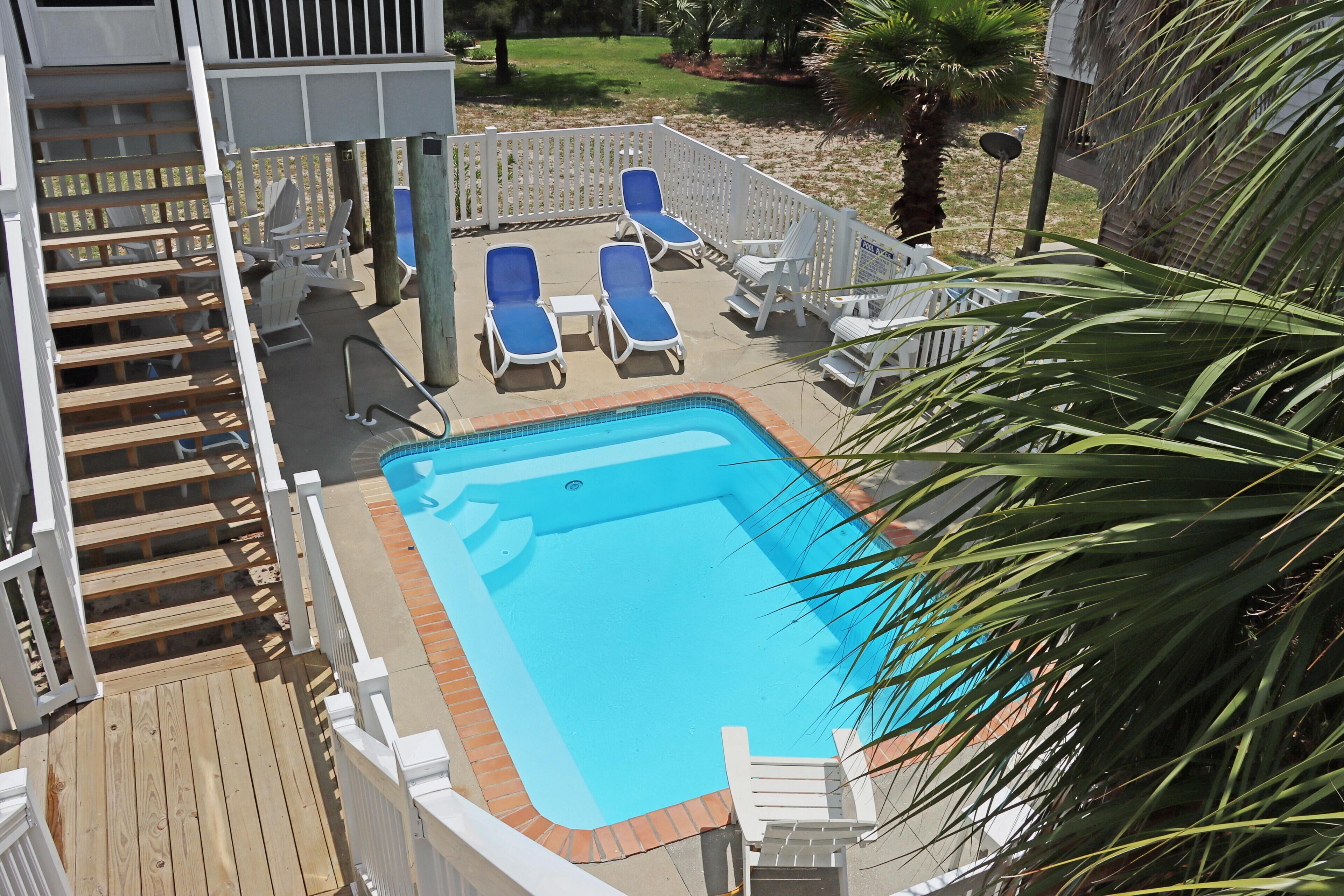 Une piscine rectangulaire à l’eau bleue, entourée d’une terrasse en bois et de rampes blanches.