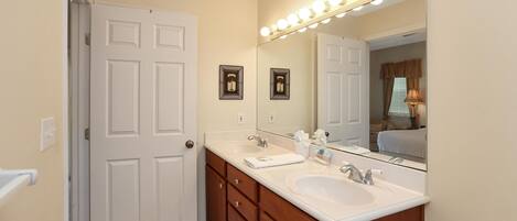 A bathroom with two sinks, a vanity, and a large mirror with lights.