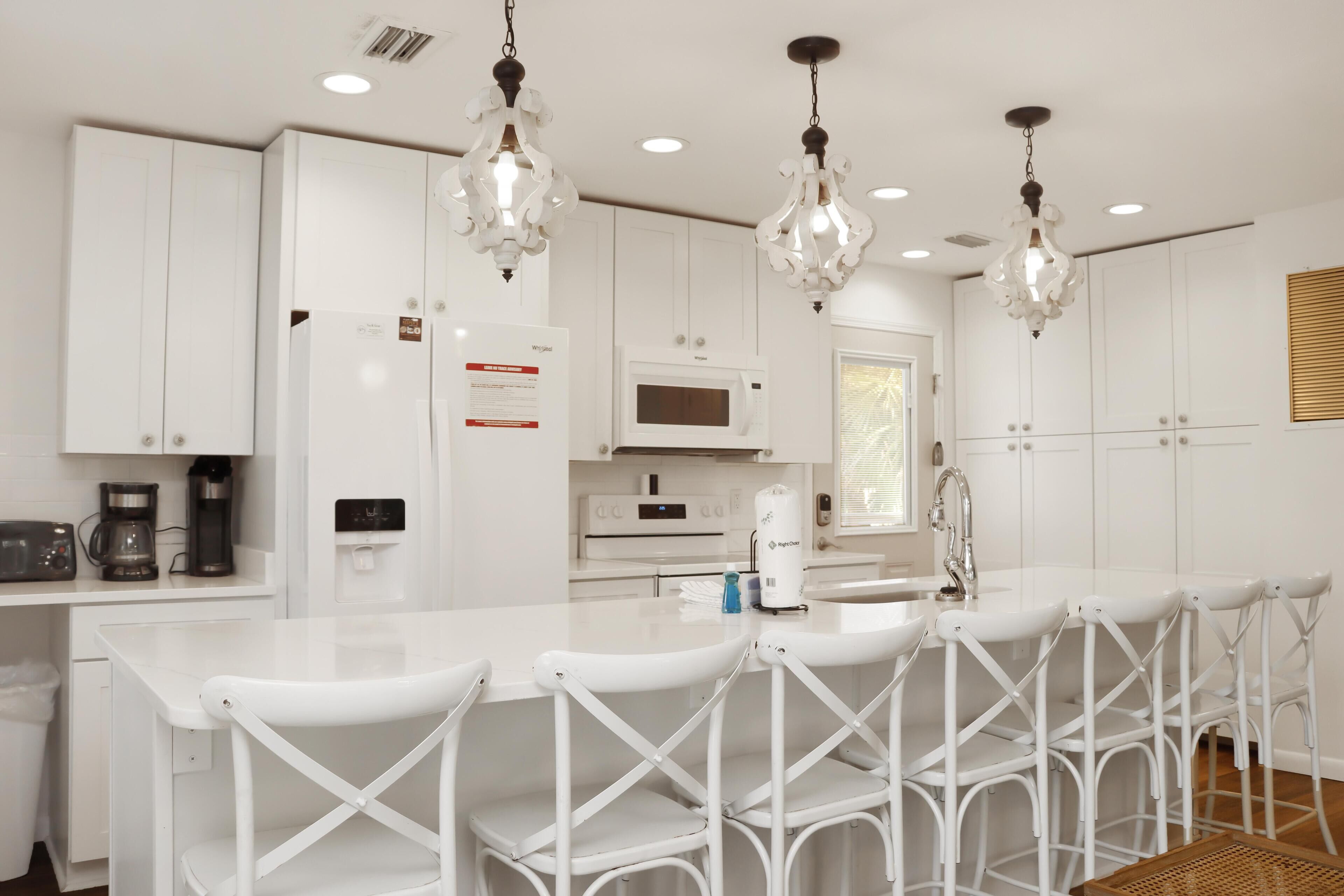 Una cocina moderna con armarios blancos, una isla central con taburetes, un microondas y una cafetera.