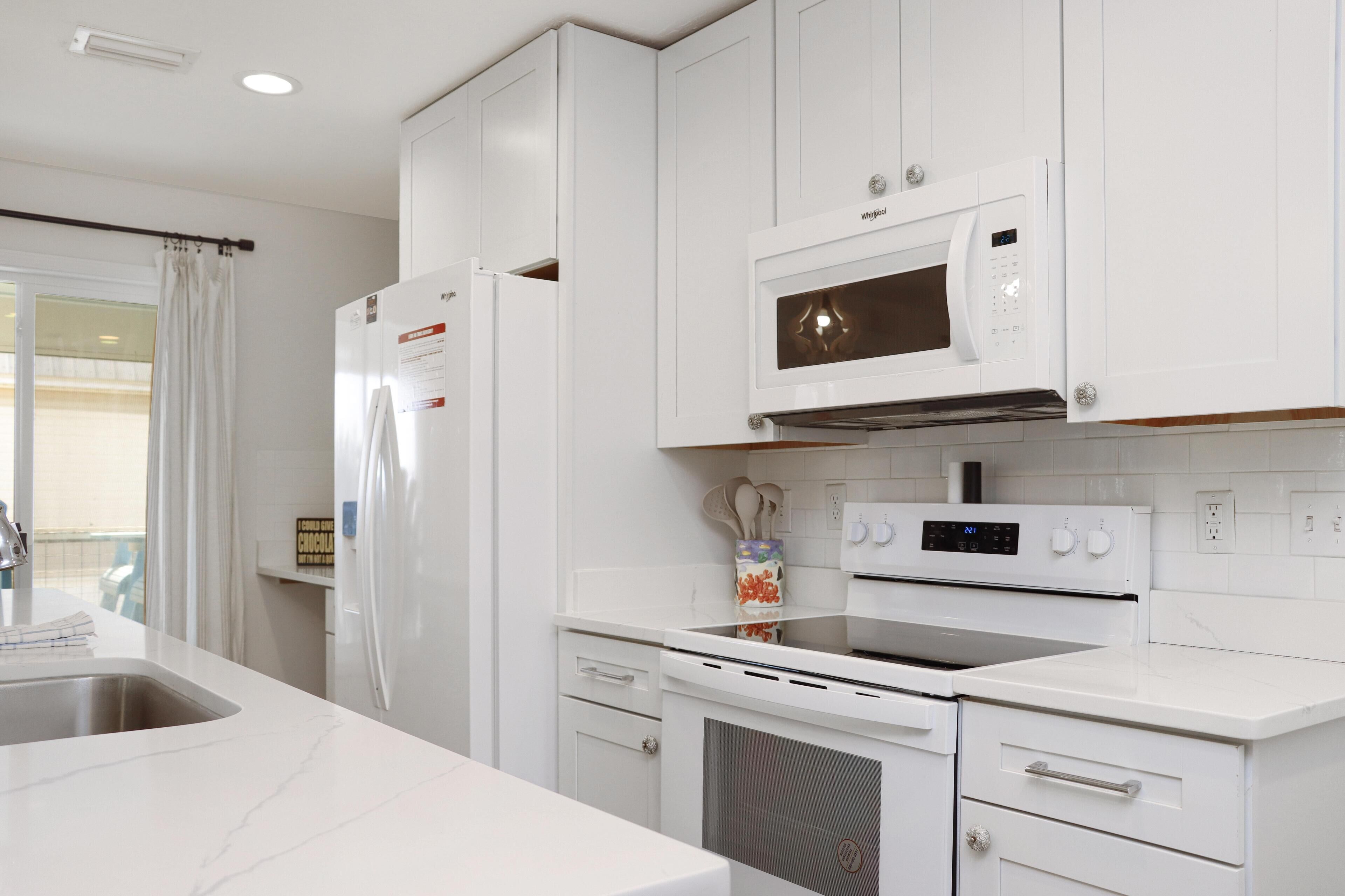 A modern kitchen with white cabinetry, a built-in microwave, an oven, and a stainless steel sink.