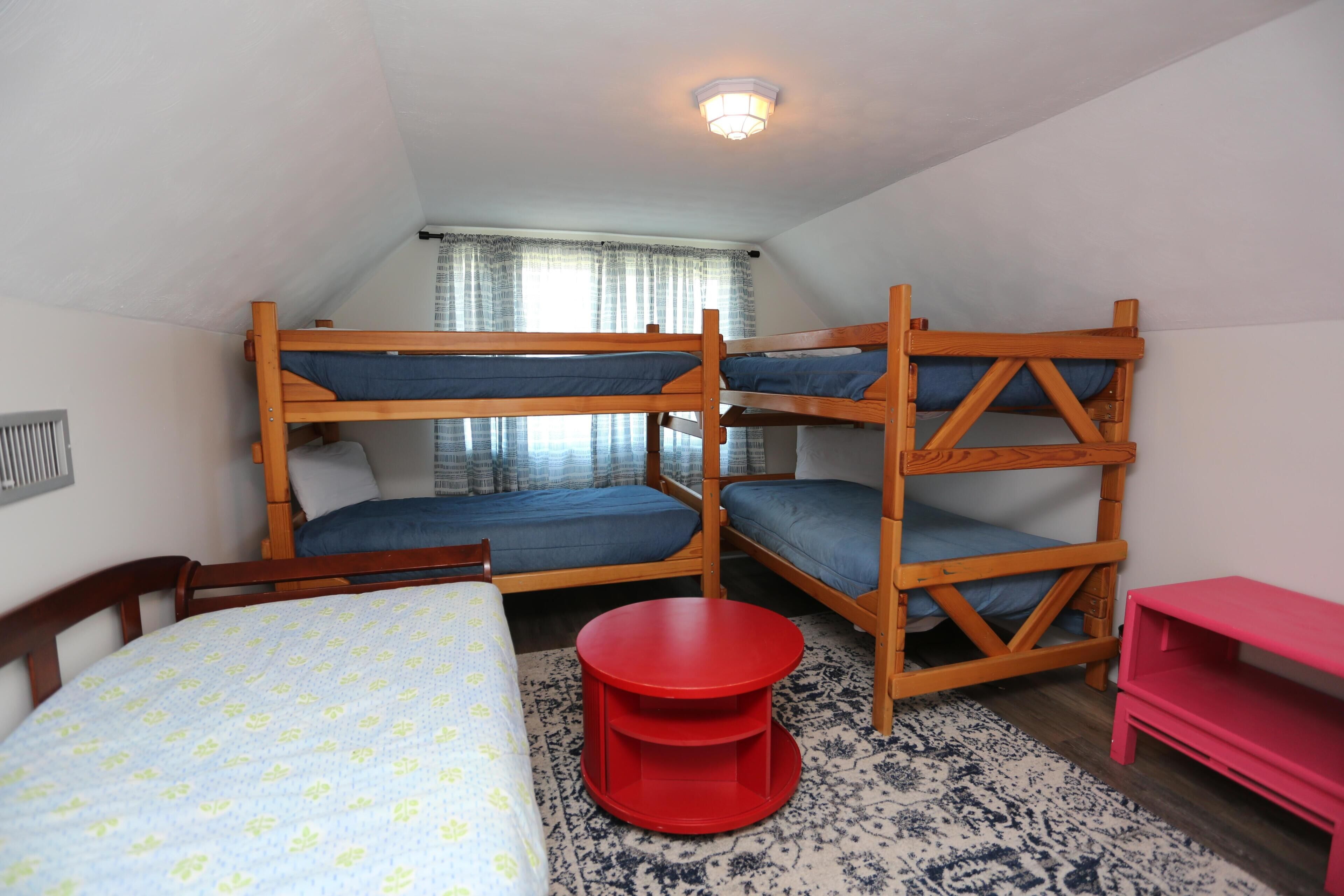 A dormitory room with bunk beds, a round red table, and a pink TV stand.