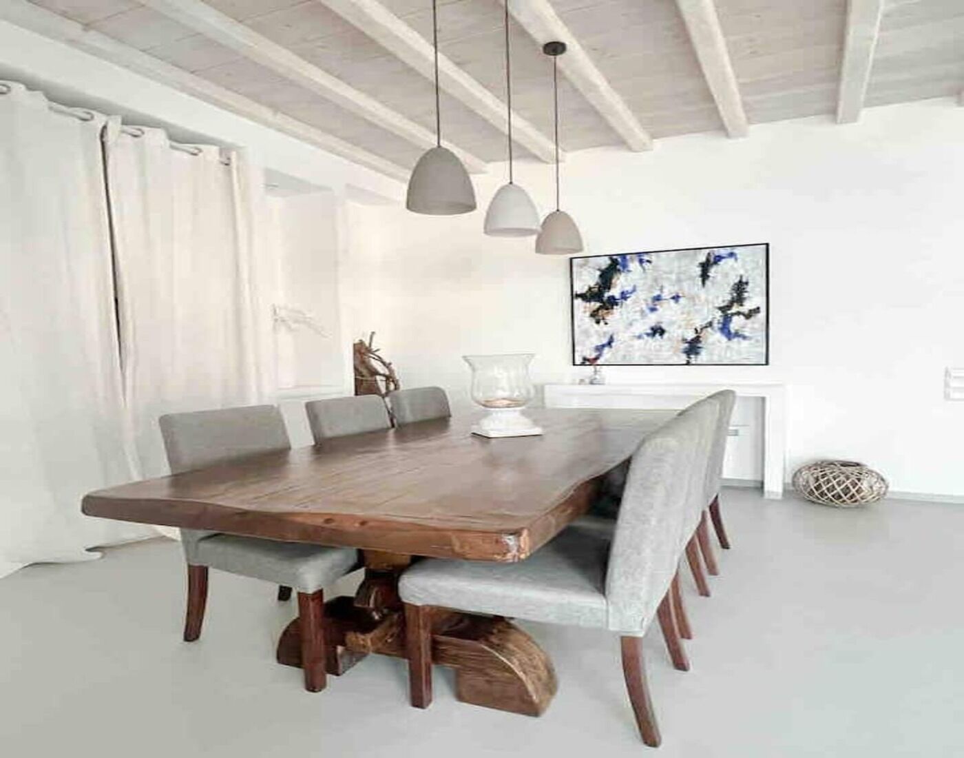 A dining area with a wooden table, grey upholstered chairs, pendant lighting, and a decorative vase.