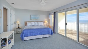 A bedroom with a bed, two bedside tables with lamps, a ceiling fan, and a large sliding glass door leading to a balcony with a view of the ocean. - Pelican Landing 3 (Port St. Joe)