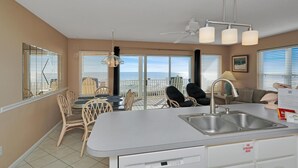 A kitchen with a large island, a dining area with chairs, a view of the ocean, and a ceiling fan. - Pelican Landing 3 (Port St. Joe)