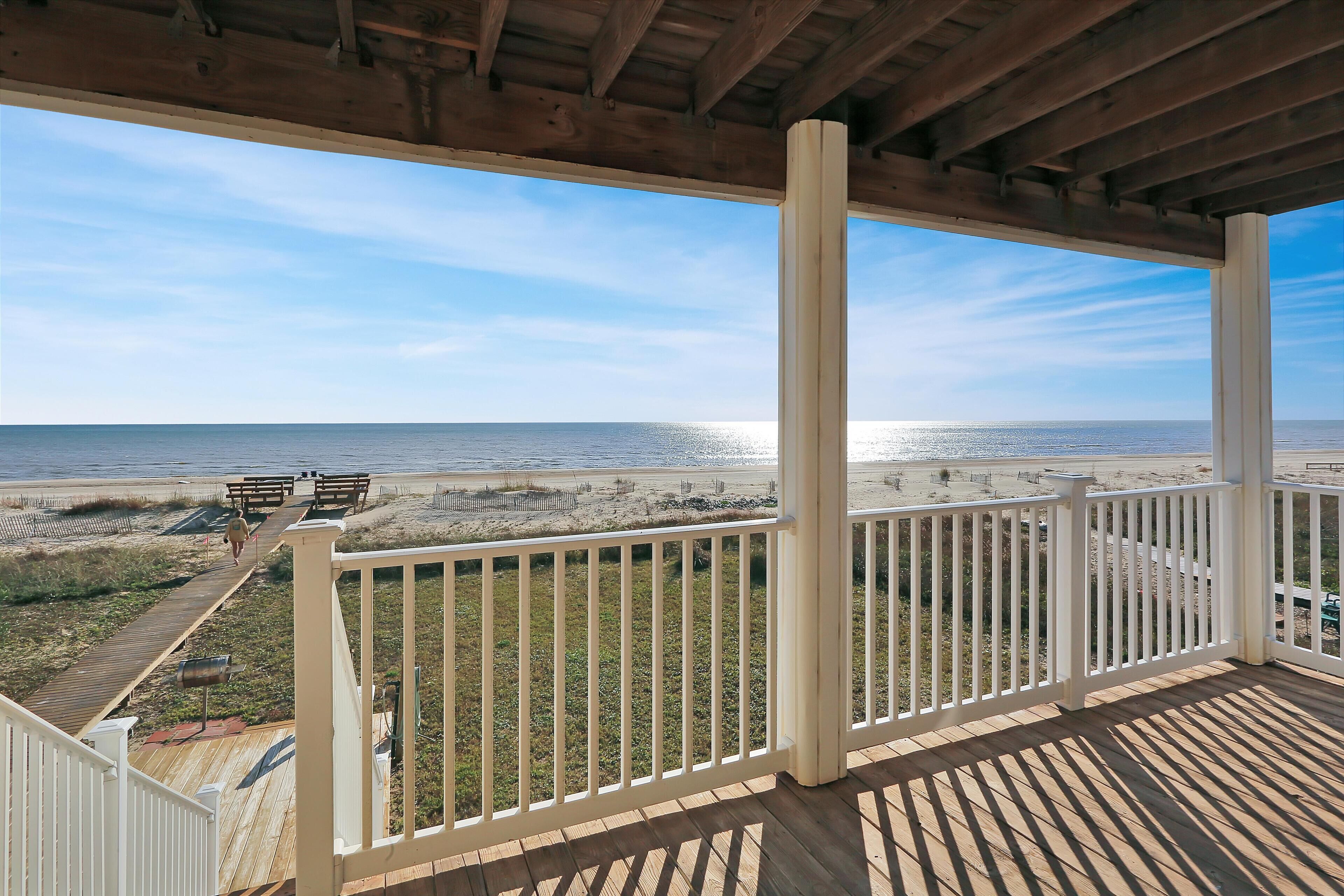 A wooden deck with white railings overlooking a beach.