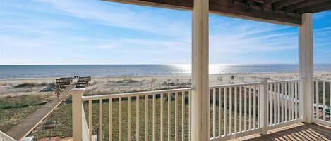 A wooden deck with white railings overlooking a beach.