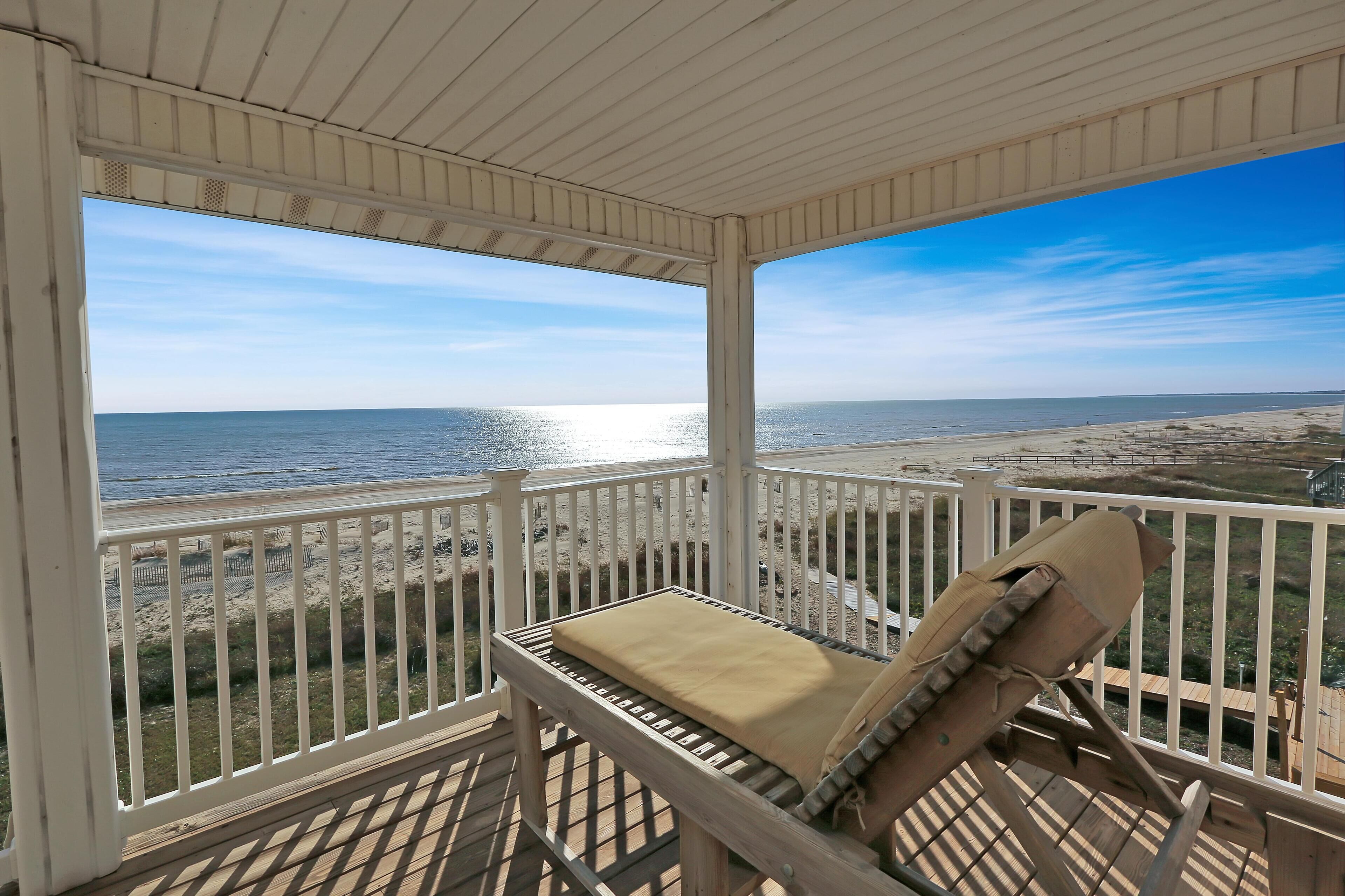 A covered deck with a view of the beach and ocean.