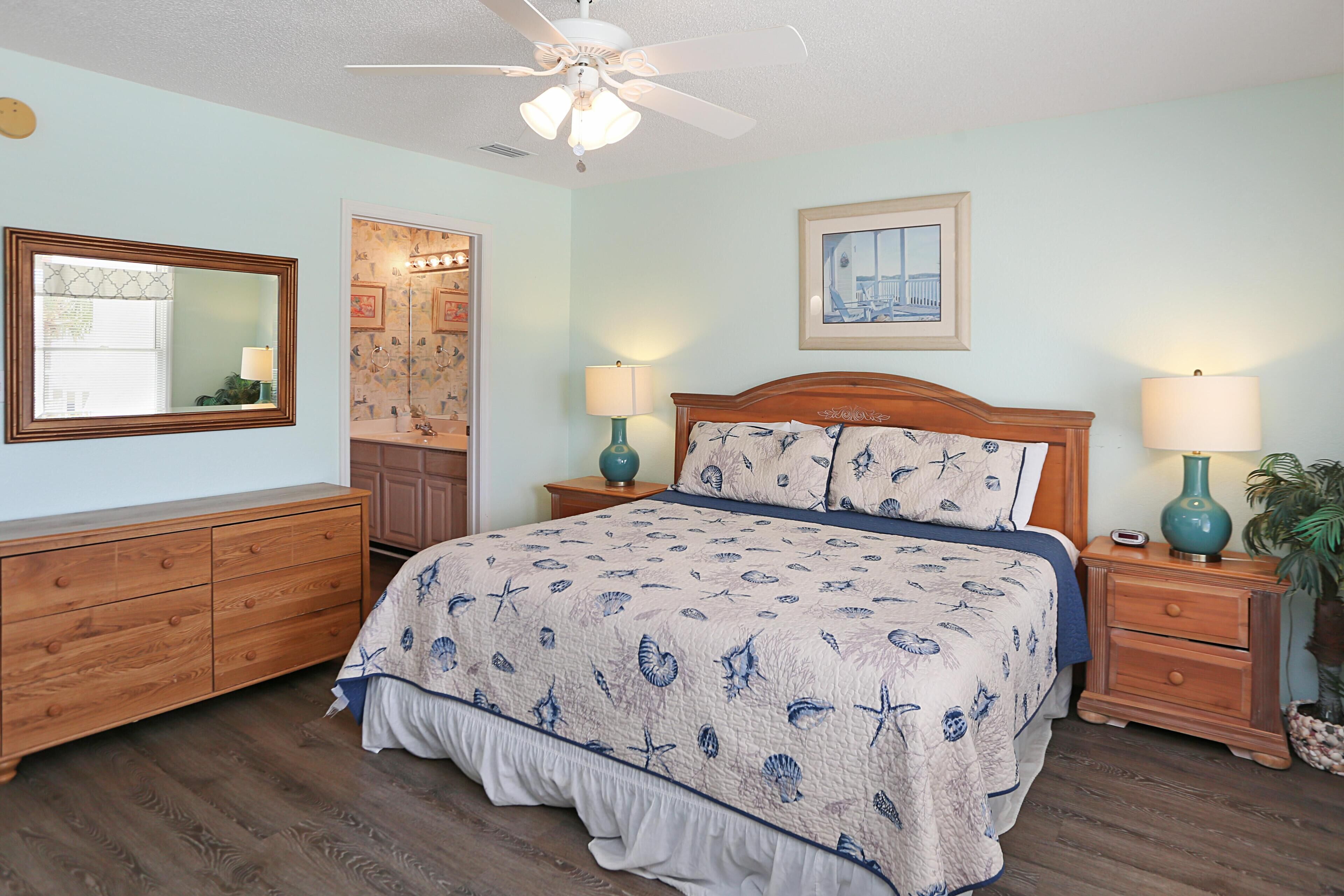A bedroom with a bed, nightstands, a dresser, a ceiling fan, and a mirror.