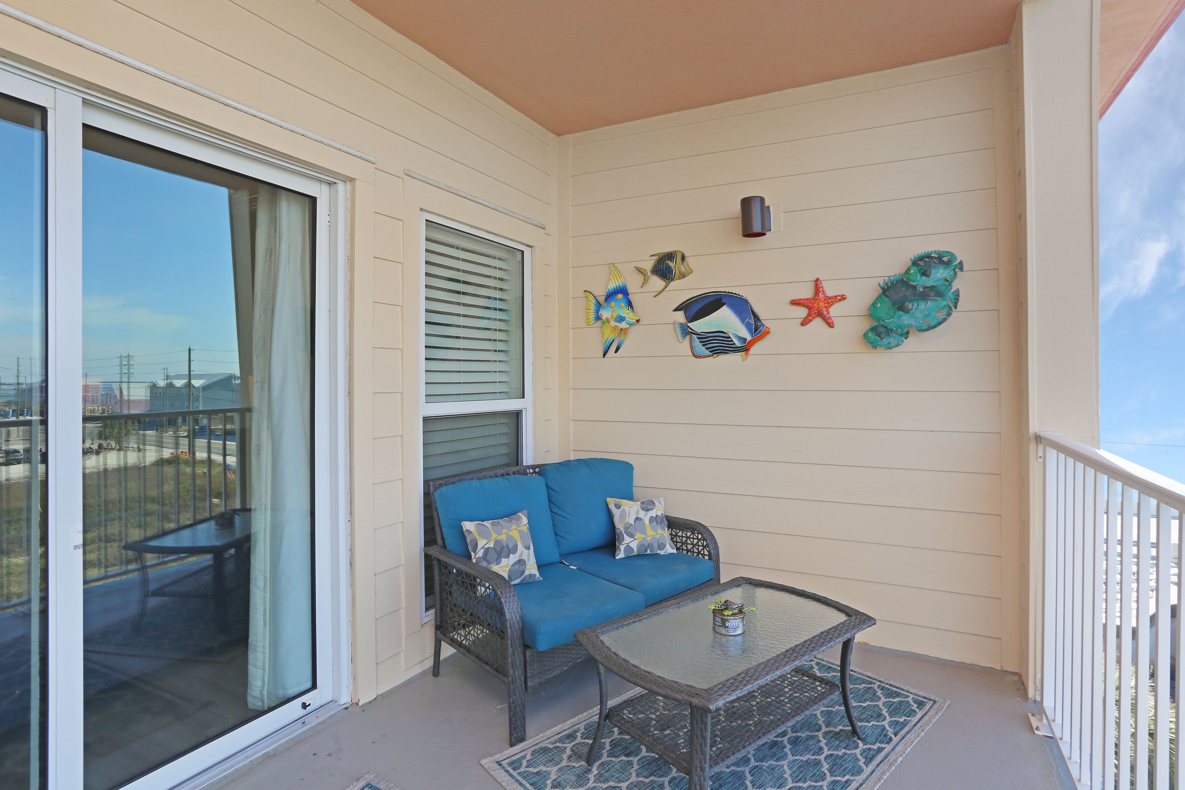Un balcon agrémenté d’un canapé bleu, d’une table en verre et de décorations murales représentant des poissons et des étoiles de mer.
