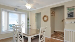 A dining area with a glass-top table and white chairs, a ceiling fan, and a clock on the wall. - Sea Cliff C-16 Gone Fishin' (Port St. Joe)