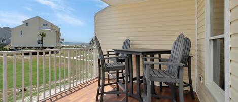 A balcony with a table and chairs, a view of the ocean, and a white fence.