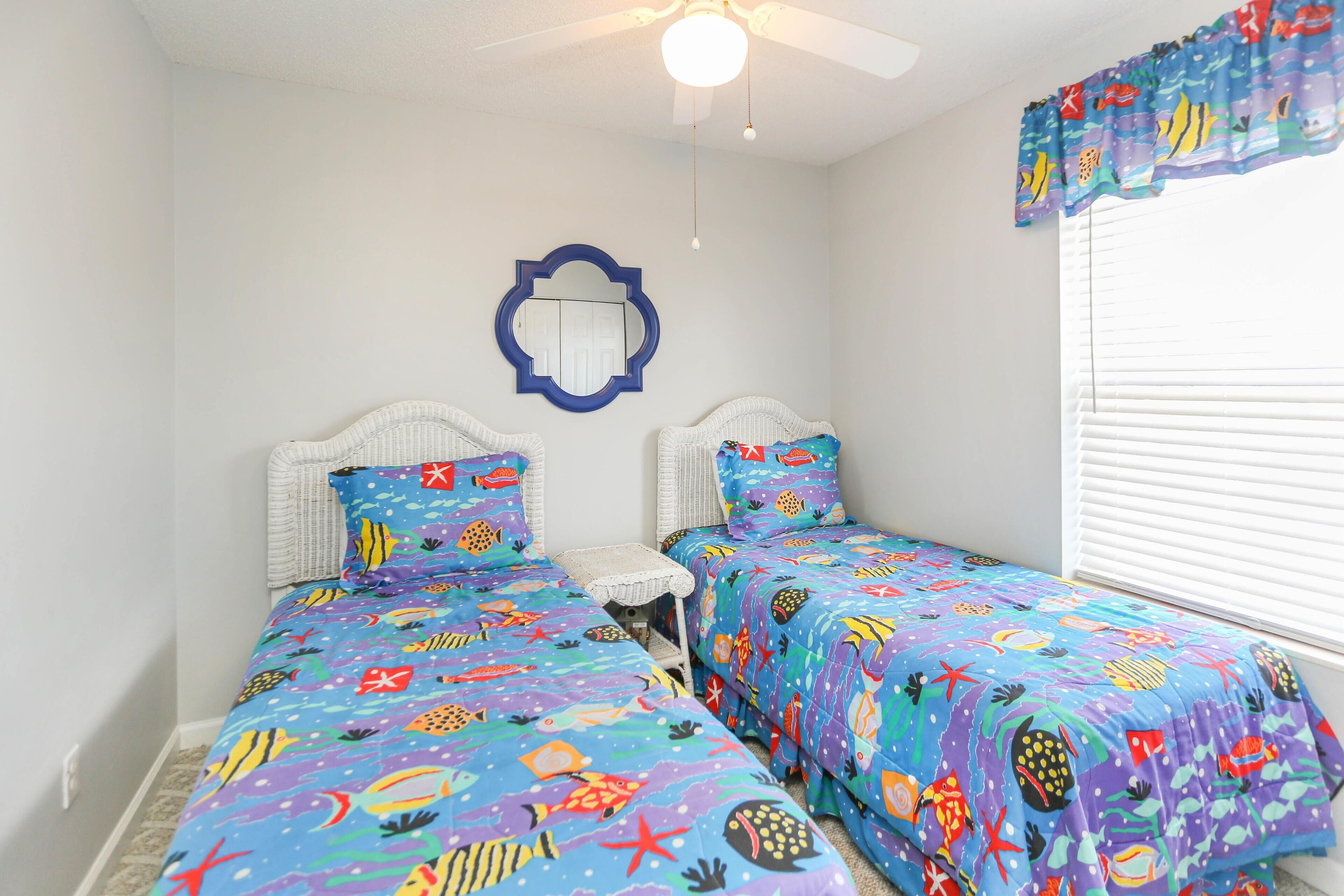 A bedroom with two beds, a ceiling fan, a mirror, and a window with blinds.