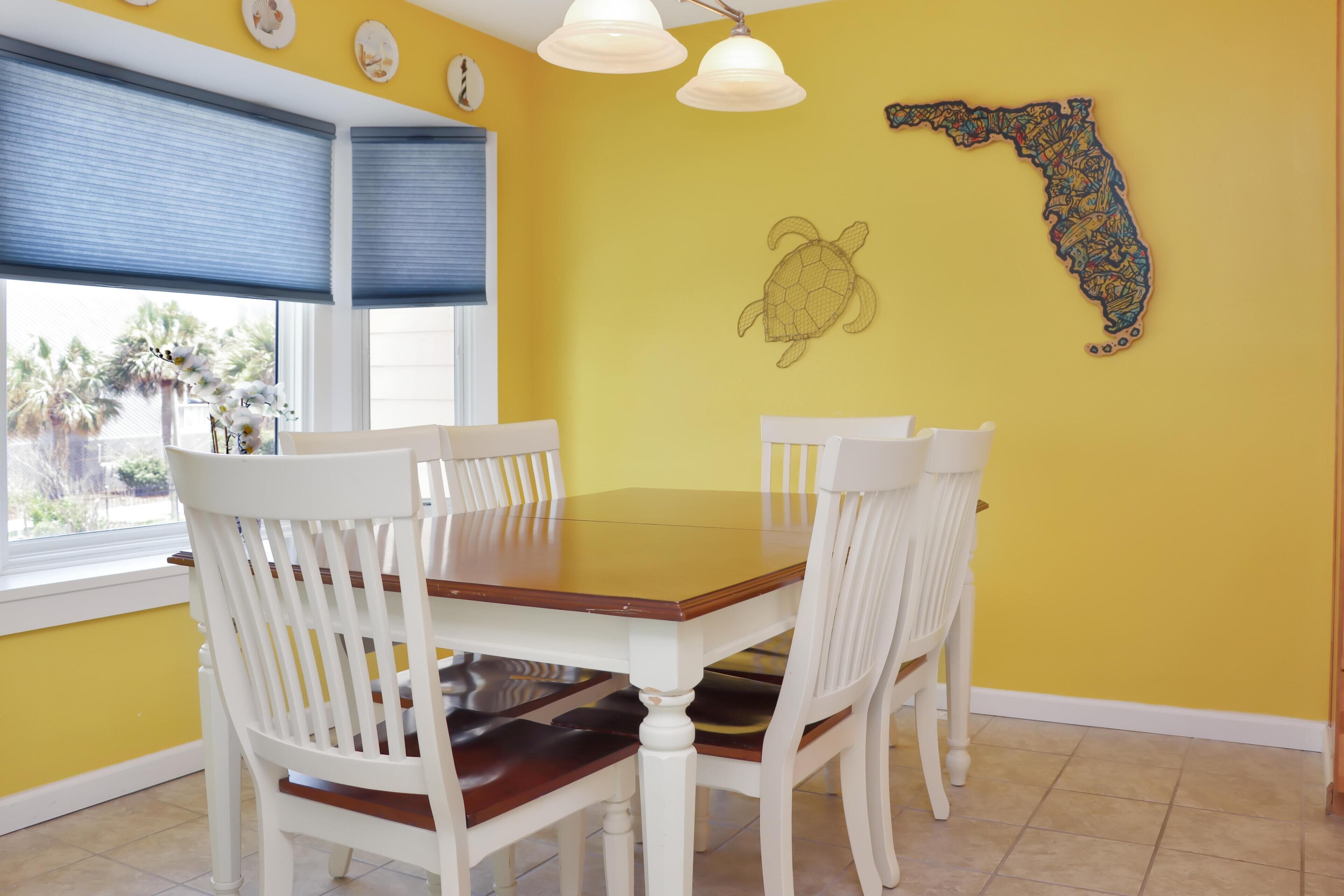 A dining area with a wooden table and white chairs, yellow walls, and a decorative map of Florida.