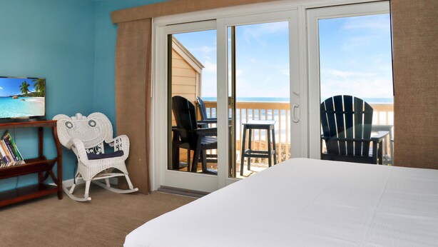 A room with a bed, a television, a rocking chair, and a balcony with chairs. - Sea Cliff B-2 (Port St. Joe)