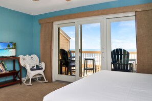 A room with a bed, a television, a rocking chair, and a balcony with chairs. - Sea Cliff B-2 (Port St. Joe)