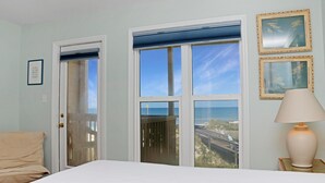 A room with a bed, a door, two windows with a view, a lamp, and framed pictures on the wall. - Sea Cliff B-2 (Port St. Joe)