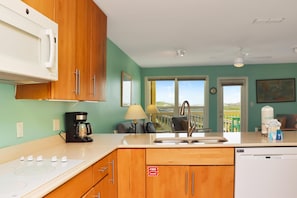 A kitchen with wooden cabinets, a built-in microwave, a coffee maker, a sink, and a dishwasher. - Sea Cliff B-2 (Port St. Joe)