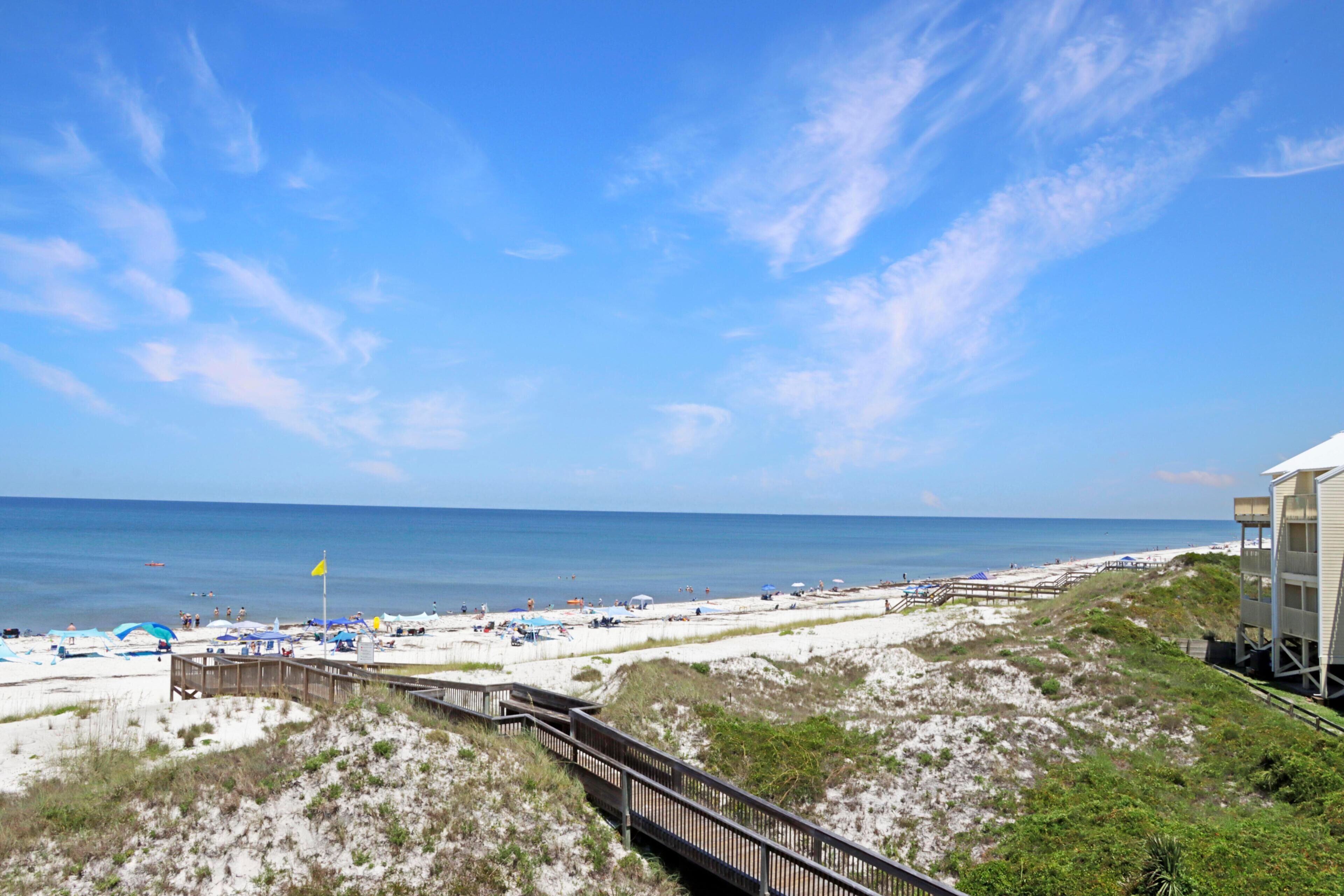 A beach with a wooden boardwalk, sandy dunes, and a clear blue sky.
