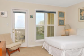 A bedroom with a bed, a chair, a lamp, and a door leading to a balcony. - Sea Cliff B-2 (Port St. Joe)