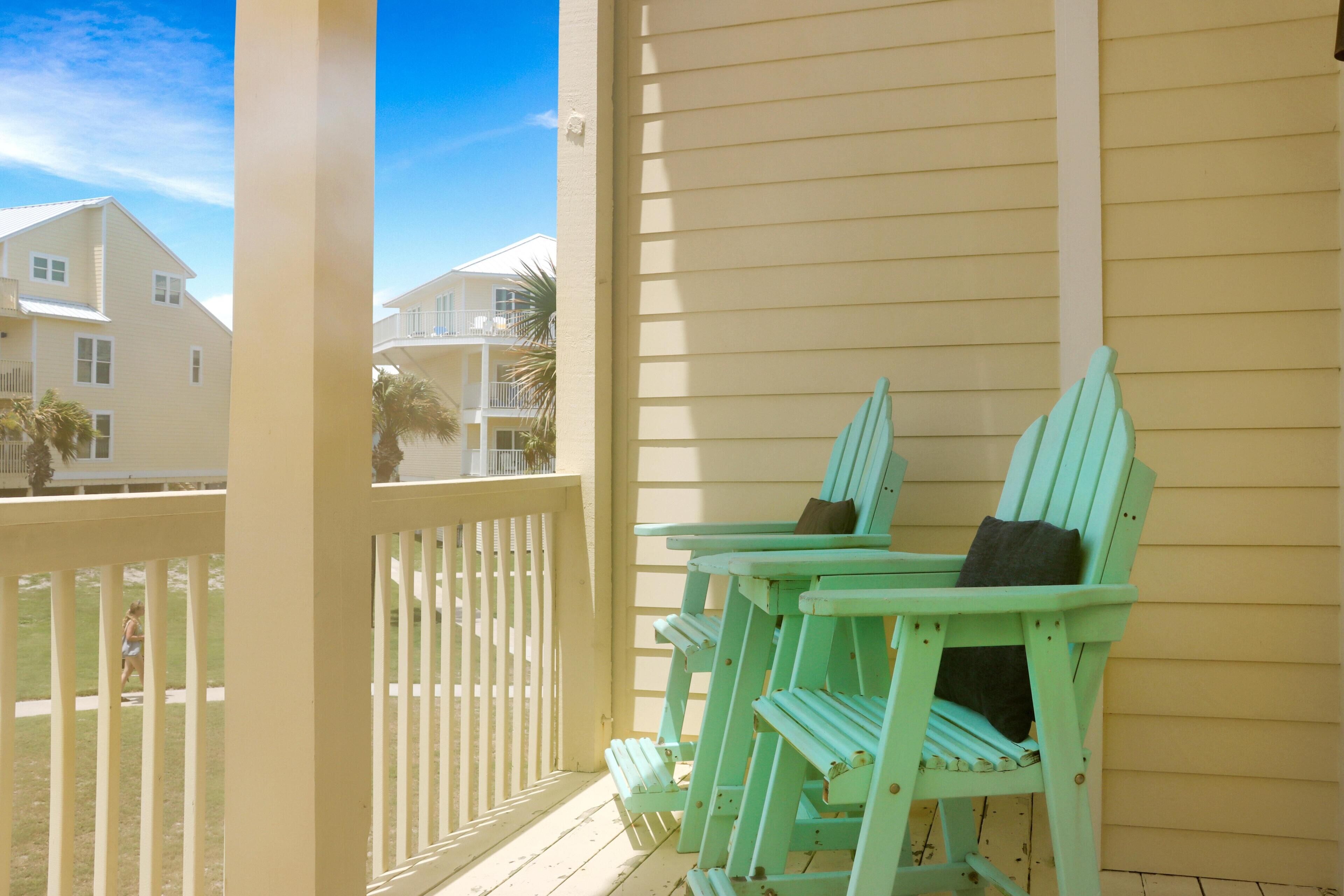 A porch with two green Adirondack chairs, a white railing, and a view of neighboring houses.