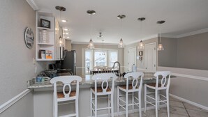 Una cocina con una isla central, taburetes blancos de barra, iluminación colgante y un reloj en la pared.