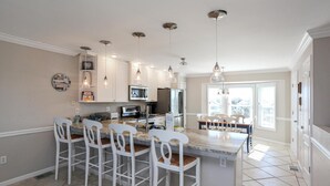 Una cocina moderna con taburetes blancos, una isla central e iluminación colgante.