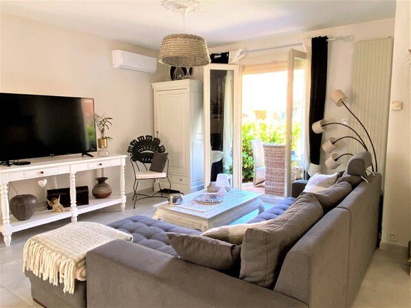 A living room with a grey sofa, a white coffee table, a TV on a white cabinet, and a wicker lamp. - 5 minutes from the beach, quiet renovated house with wifi, air conditioning and jaccuzi (CANET EN ROUSSILLON)