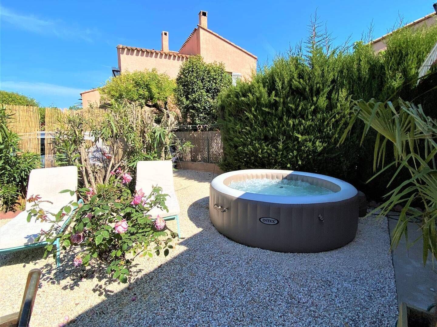 A hot tub in a garden with gravel ground, surrounded by plants and a wooden fence.