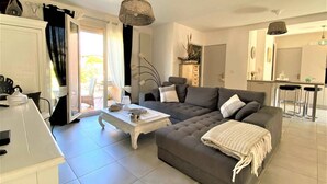A modern living room with a grey sofa, a white coffee table, and a dining area with a bar. - 5 minutes from the beach, quiet renovated house with wifi, air conditioning and jaccuzi (CANET EN ROUSSILLON)