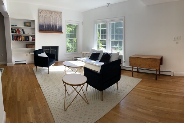 Uma sala de estar com sofá, duas poltronas, mesa de centro, estante de livros e lareira.