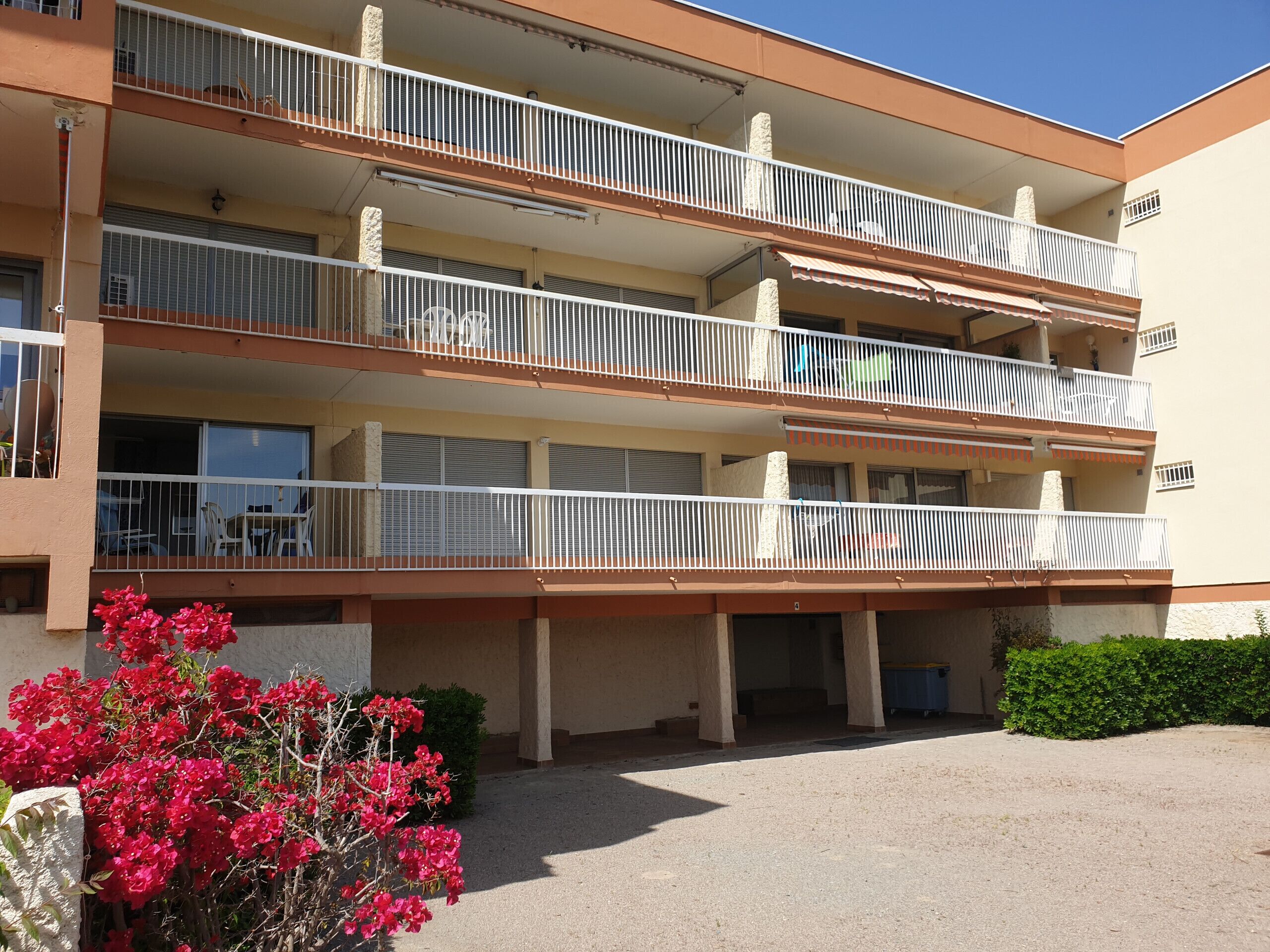 A multi-story building with balconies, a covered outdoor area, and a garden with red flowers.