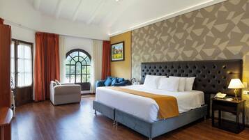 A hotel room with a large bed, a sofa, a desk, and a window with curtains.