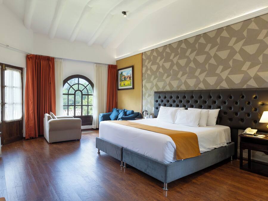 A hotel room with a large bed, a sofa, a desk, and a window with curtains.
