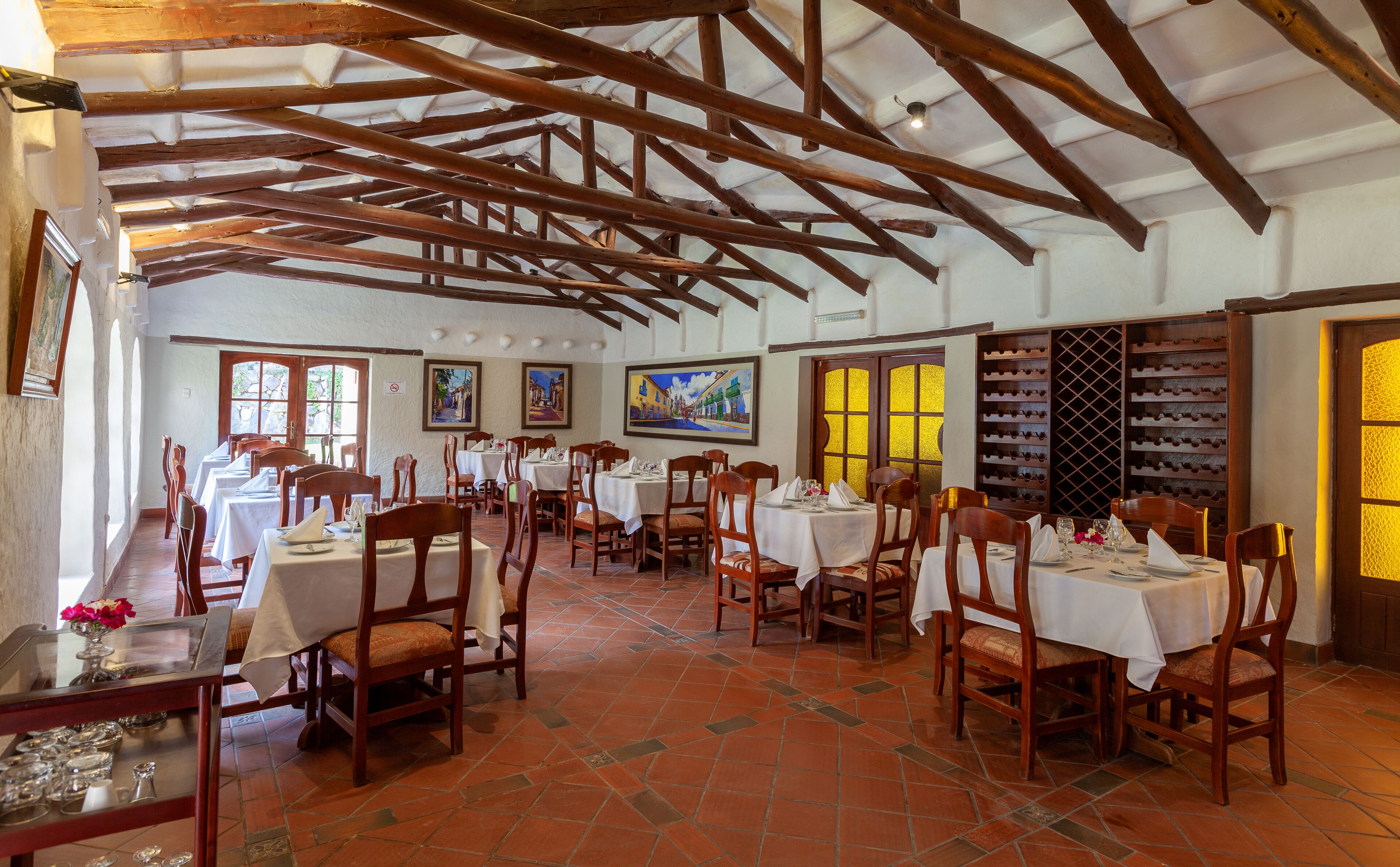 A restaurant with wooden beams, tiled floors, and white tablecloths.